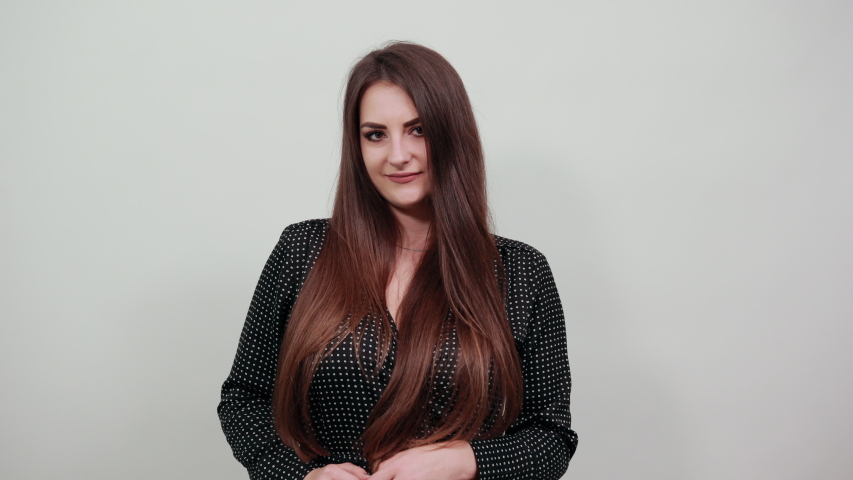 Caucasian woman over isolated gray background wearing casual black dress with white polka dot, doing shape of heart, lookin at camera. People lifestyle concepte.