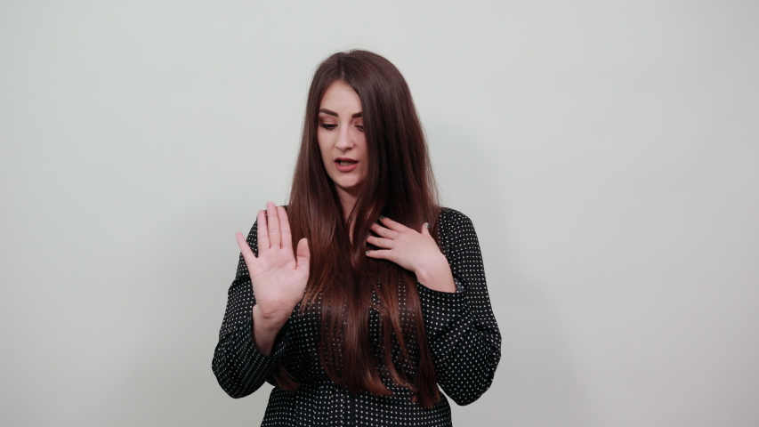 Unhappy youg woman over isolated gray background wearing casual black dress with white polka dot, showing palms at camera, doing NO, stop gesture. People lifestyle concepte.