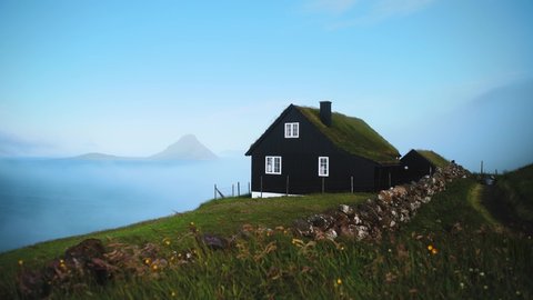 Foggy morning view of a house with typical turf-top grass roof and blue sky in the Velbastadur village on Streymoy island, Faroe islands, Denmark. UHD 4k video