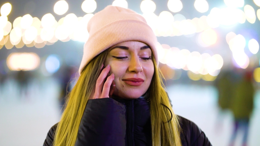 Positive girl in winter outfit talking on phone near skating rink