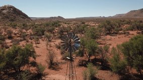 4K aerial drone video of farm wind water pump on pillar, red stone gravel plains, wide dry bush savanna panorama near town Grunau, Namibia, B1 desert highway near RSA border, southern Africa