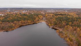 Aerial footage over Härlanda Tjärn lake in Gothenburg, Sweden. Birds eye view Showing the beautiful nature fall colors trees and the big water lake as outdoor nature scene with city view in background