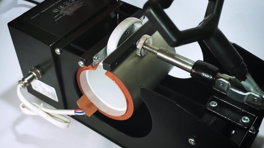 The black thermopress for cups, mugs is intended for transfer of the image or photo (sublimation). Сlose-up of a mug clamped in the thermopress. The process of transfer of the image on mugs, cups., a Business & Finance Video by Uliks-Uliks