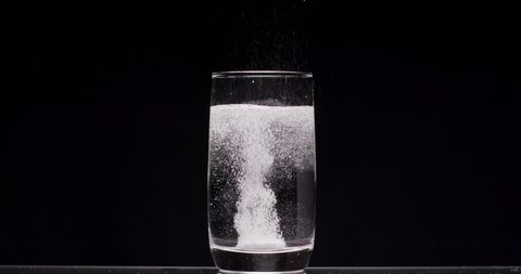 patient throws aspirin into a glass of water on a black background Pill falling down in glass with water. Slow motion