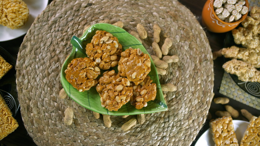 Closeup shot of peanuts chikki with roasted groundnuts - Lohri celebration in India. Beautifully plated peanuts chikki rotating on a turntable and surrounded by rewri, gajak, murmura laddu, etc con...