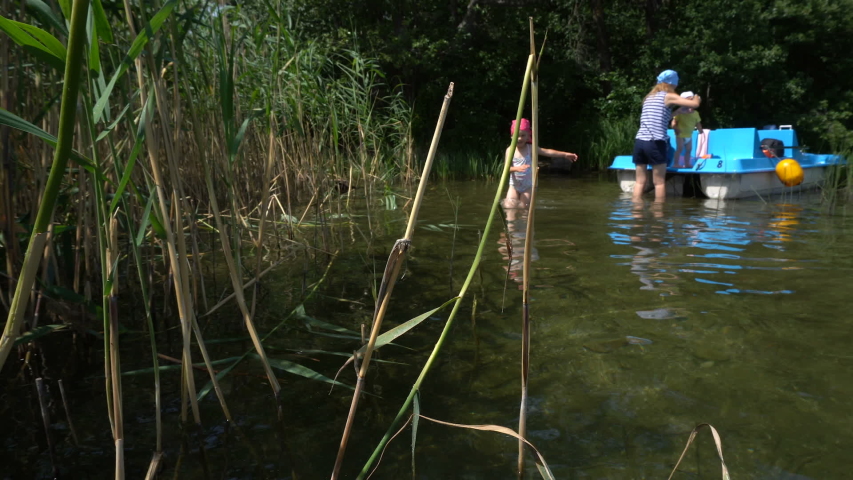 4 years old girl wade in water and mother with little brother near catamaran. Gimbal motion shot.