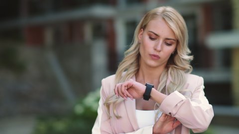 Close up young woman looking at smart watch at street. Portrait of worried businesswoman waiting smart clothing outdoors. Concerned woman looking at wrist watch outdoors.