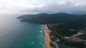 Flying in the evening along the Karon beach towards the mountains on the island of Phuket in Thailand, a tourist area top view. Aerial video