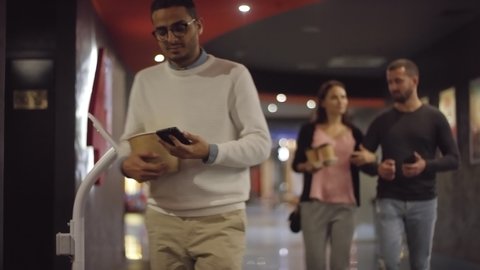 Tracking shot of people with smartphones using digital movie tickets to enter cinema auditorium before watching movie