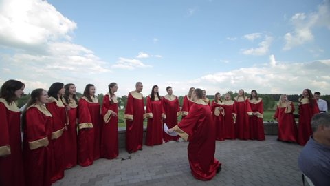 Minsk, Belarus - August 24, 2019: Big choir of people of different age clapping and singing cheerfully with a conductor in summer outdoor