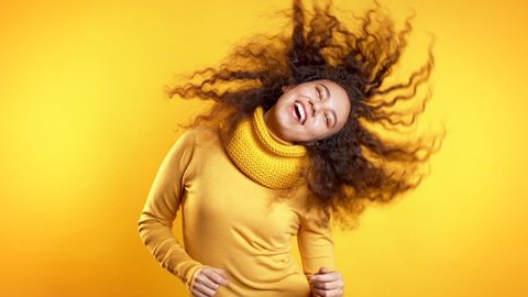Young cute girl smiling and dancing on yellow studio background. Woman in colorful bright wear. Positive mood. Slow motion.: film stockowy
