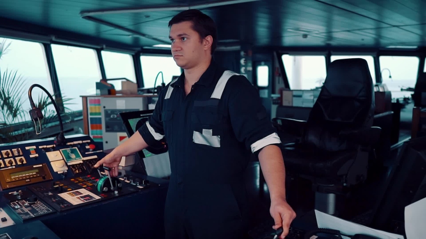 Marine navigational officer during navigational watch on Bridge . He is maneuvering the ship. Work at sea.