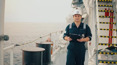 Marine chief officer or chief mate on deck of ship or vessel. He fills up ahts vessel checklist. Ship routine paperwork. He holds VHF walkie-talkie radio in hands.