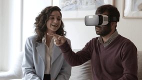 Smiling young woman presenting goods with help of VR technology. Cheerful Caucasian man wearing virtual reality headset and talking with woman while sitting on couch. VR technology concept