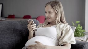 Smiling pregnant woman having video call via smartphone. Cheerful expectant mother talking to interlocutor through phone. Pregnancy concept