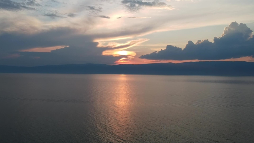 The drone gradually flies over the surface of the water. Lake Baikal, nature of Russian Federation. Panoramic Aerial Video Shot of sunset. Blue crystal water. 