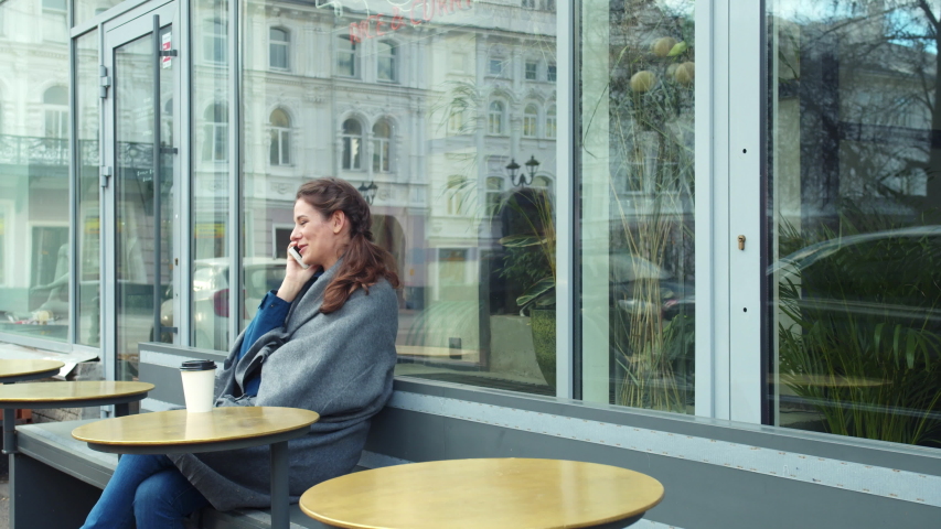 Girl in grey blanket sit outside and talk on phone