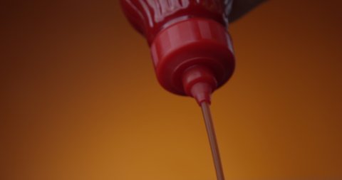 Ketchup is Pouring out of a Red Bottle a Close Up on a Terracotta Background