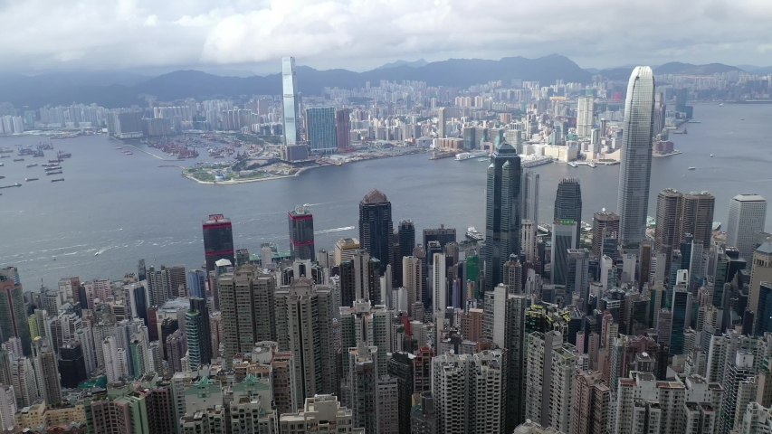 Aerial panorama of Hong Kong viewed from top of Victoria Peak with skyscrapers on HongKong Island  in Kowloon Downtown by Victoria Harbour  residential towers on Mid-Levels hillside under cloudy sky