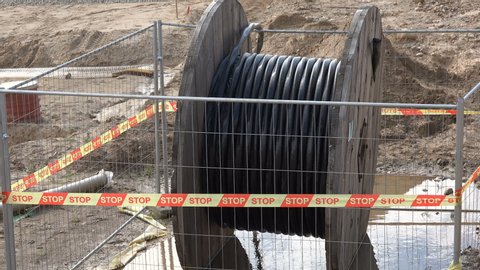 High voltage cable reel in wet dirt. Laying electricity and communication cables underground under highway road.