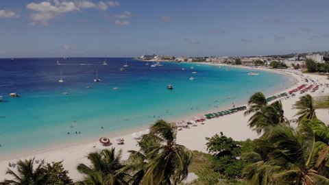 Aerial of the beautiful beach in Barbados. Drone flying dolly over palm trees, beach blue water and boats 