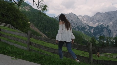 female traveler is walking near fence of meadows in Alps, looking on mountains in summer in Slovenia ஸ்டாக் வீடியோ