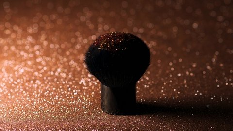 Lush makeup brush and gold sequins. A woman's hand touches the pile and makes a cloud of sequins