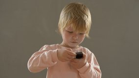 Cute blond boy in pink pajamas plays with smartphone touching touch screen with finger. child wants to quickly become adult and learn everything. Home teaching concept for lagging children
