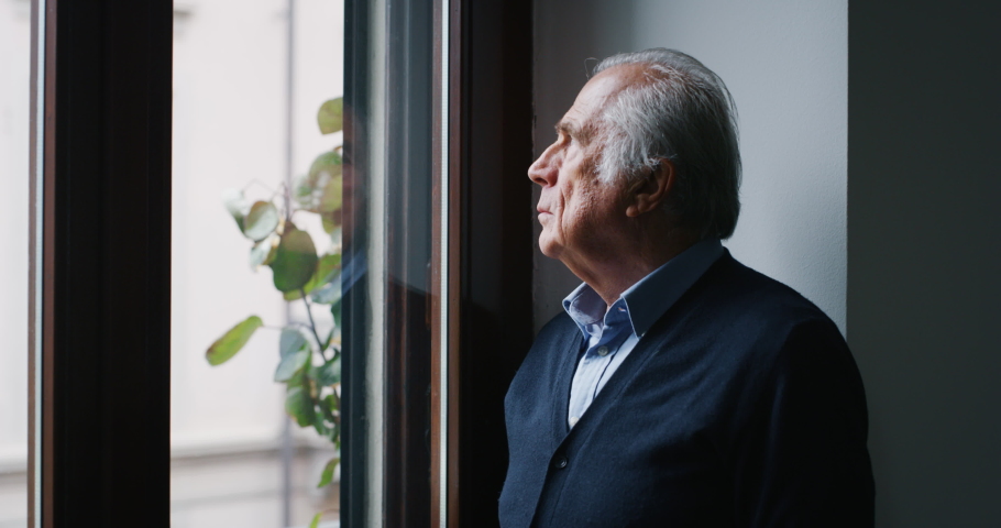 An elderly thoughtful smiling man is looking out a window of his house in the morning. Royalty-Free Stock Footage #1043609086