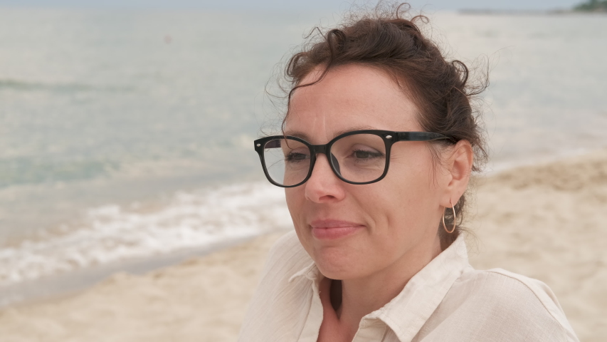 Pleased women by the sea. Joyfull female in glasses admires the sea on the beach.