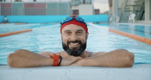 Happy bearded muscular swimmer smiling after his morning training in olympic swimming pool. Slow motion 4k video, closeup
