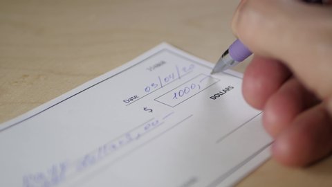 Close-up of a man's hand filling out a 1,000 dollars'Bank check.