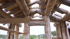 Bottom view of a new home under construction and its unfinished roof on bright cloudy sky background. Clip. View inside of the house made of timber.