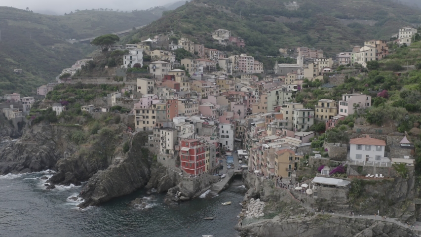 Aerial view of Riomaggiore Bay village. Colorful italian houses on rocky coast. Boats floating in the sea. Foaming waves breaking on stones. Chinque Terre, Italy. 