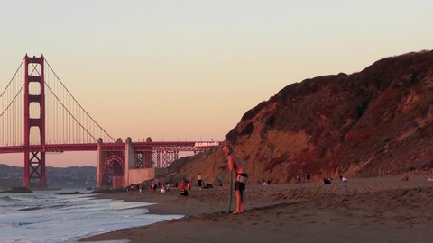 Unidentified people on the Baker Beach in San Francisco at sunset, with the Golden Gate Bridge in the background, 2018