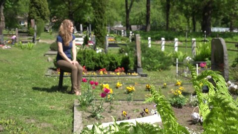 Sorrow widow woman girl sit shrink on bench near father husband tomb in graveyard. Fern plant. Static focus change shot. 4K