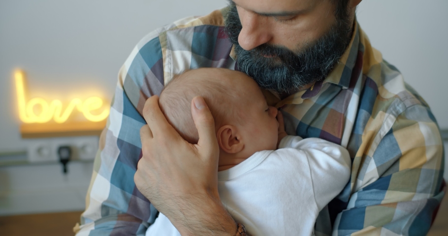 Bearded young father gently hugs a newborn sleeping baby in his arms. Gental parenting and family love concept. Rocking baby with fitball jumping. Royalty-Free Stock Footage #1043660881