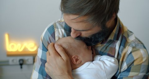 Bearded young father gently hugs a newborn sleeping baby in his arms. Gental parenting and family love concept. Rocking baby with fitball jumping.