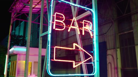 Neon bar sign medium shot . Night exterior video footage of vintage neon sign. A nighttime exterior shot of a generic, unbranded bar and restaurant in street . Gimbal shot .