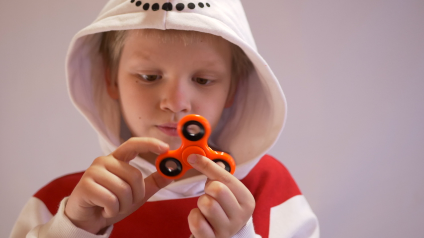Funny blond child in nowman costume twists spiner on his nose. Portrait of boy on black background. 4K. Soothing toy. Autism. Exercise for Preschoolers