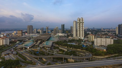 Aerial time lapse of Johor Bahru city with tall buildings in clear sky at sunset and busy traffic on elevated highway leading to CIQ. Day to night.  Zoom out motion timelapse. Prores Full HD.