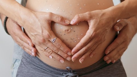 Mommy and daddy hands on pregnant tummy with stars, white background. Pregnant couple caressing pregnant belly. Happy pregnancy, motherhood, maternity. Gental parenting concept Close-up. 4K UHD,slowmo