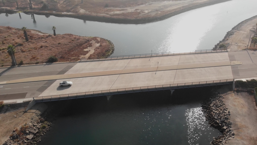 Slow aerial pull back from Long Beach CA bridge with autos and blue canal