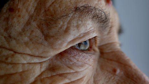 The face and eyes of an old man. Large wrinkles on the face of an old woman. Face close up. A senior citizen looks into the distance.