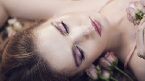 Face of beautiful girl with rose. Women lies in roses. Delicate scarlet roses and a woman. Aromatherapy. Valentine's Day. Natural cosmetic. Gentle perfume.