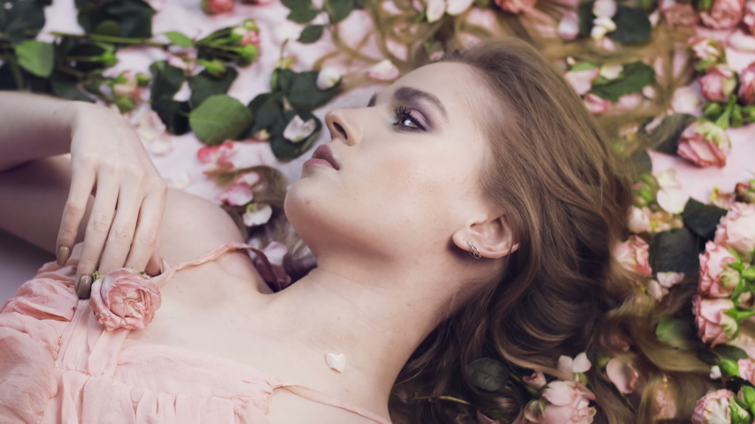 Beautiful girl lies in roses. Delicate scarlet roses and a woman. Aromatherapy. Valentine's Day. Natural cosmetic. Gentle perfume. | Shutterstock HD Video #1043707651