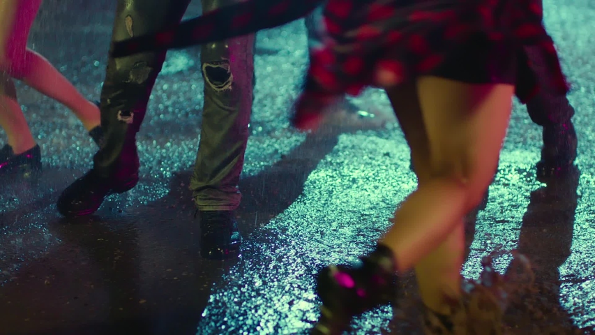 Footage of young people's feet and legs jumping and dancing in the rain at night. 