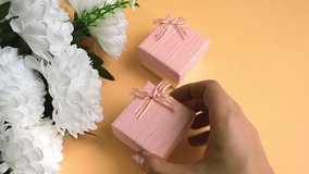 Caucasian young female hand places pink gift boxes next to a white bouquet of flowers. Golden ribbon decorations. Peach color background. - Powered by Shutterstock - Get 15% off with code: PIKWIZARD15
