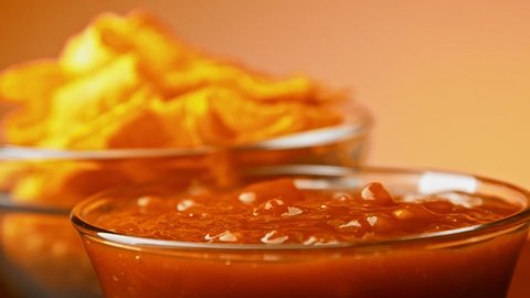 Hand dips tortilla chip into salsa sauce slow motion close-up