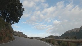 4K point of view footage: car driving on countryside road through beautiful mountain landscape with pine and olive trees, rocks, meadows. Travel by typical Mediterranean countryside. Mallorca, Spain